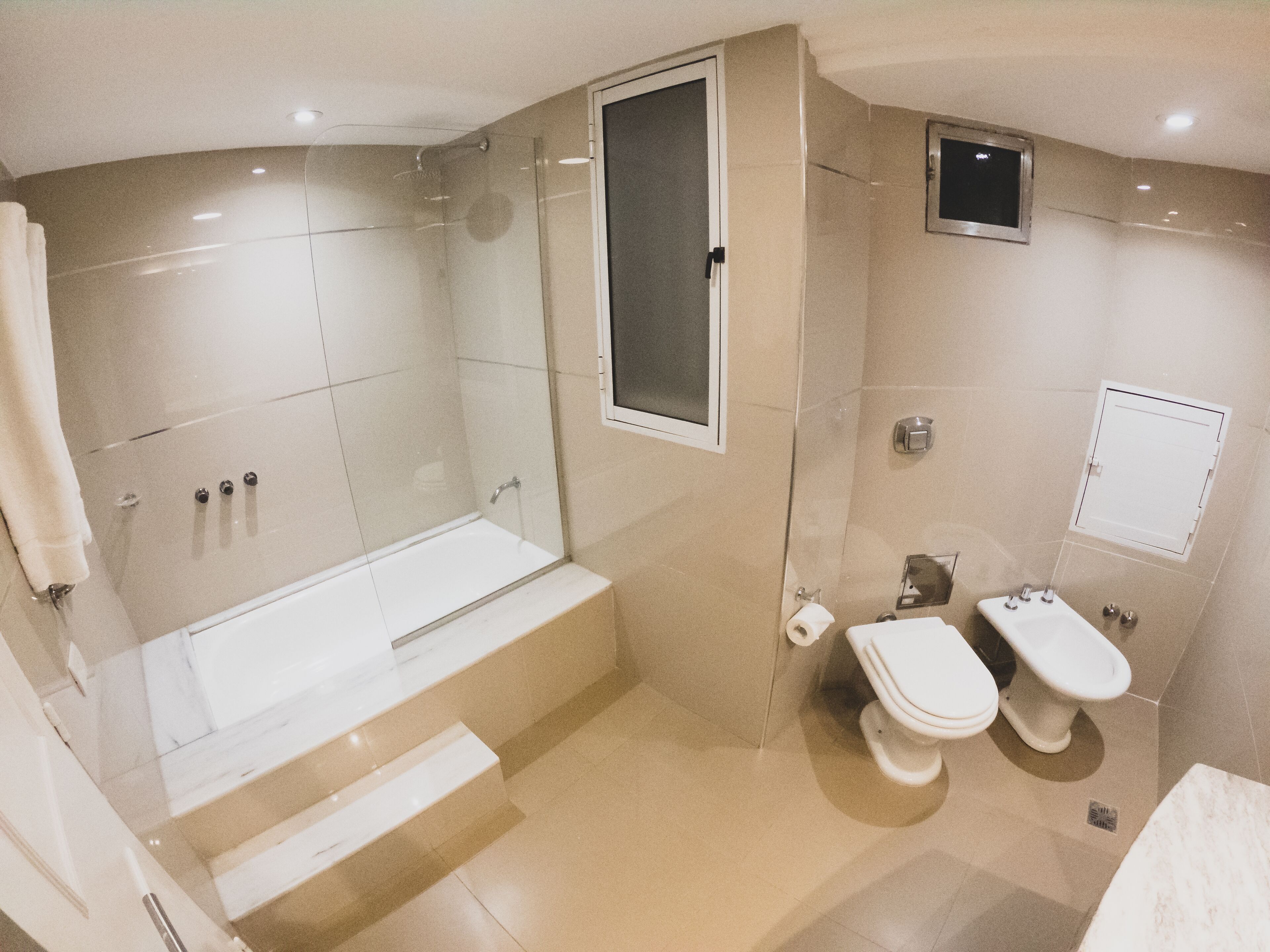 Ein modernes Badezimmer mit einer gläsernen Duschkabine, einer Badewanne, zwei Toiletten und einem Waschbecken.