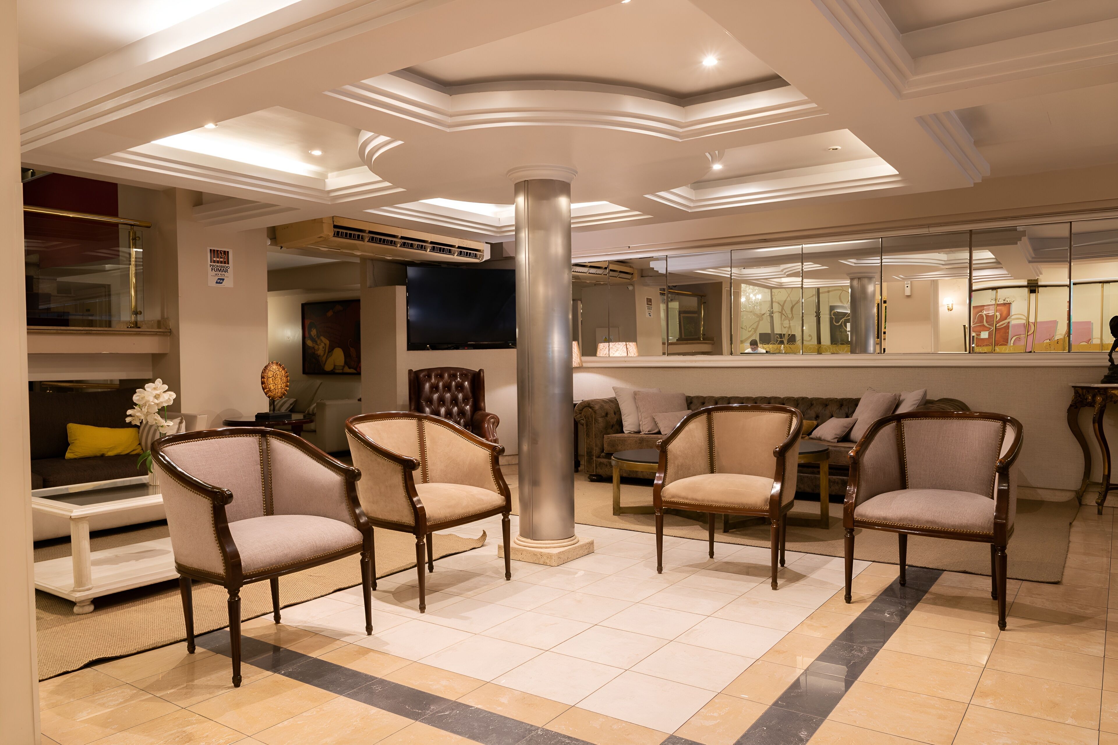 Eine Lobby mit einer zentralen Säule, einer Sitzecke mit Sesseln, einem Sofa und einem Fernseher.