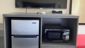 Une petite cuisine équipée d’un réfrigérateur en acier inoxydable, d’un four à micro-ondes et d’un téléviseur à écran plat fixé au mur.