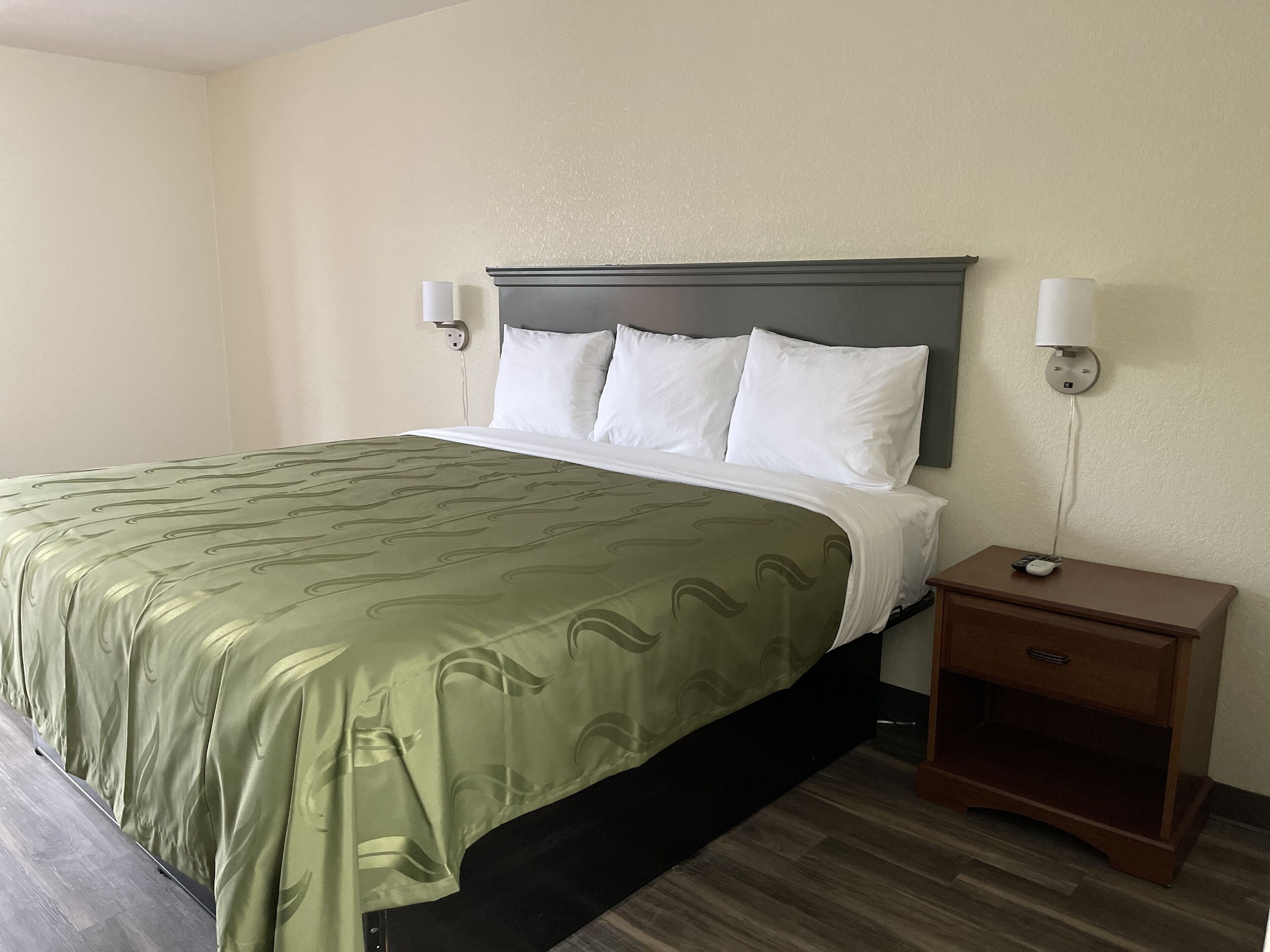 A hotel room with a bed, a nightstand, and a wall-mounted lamp.