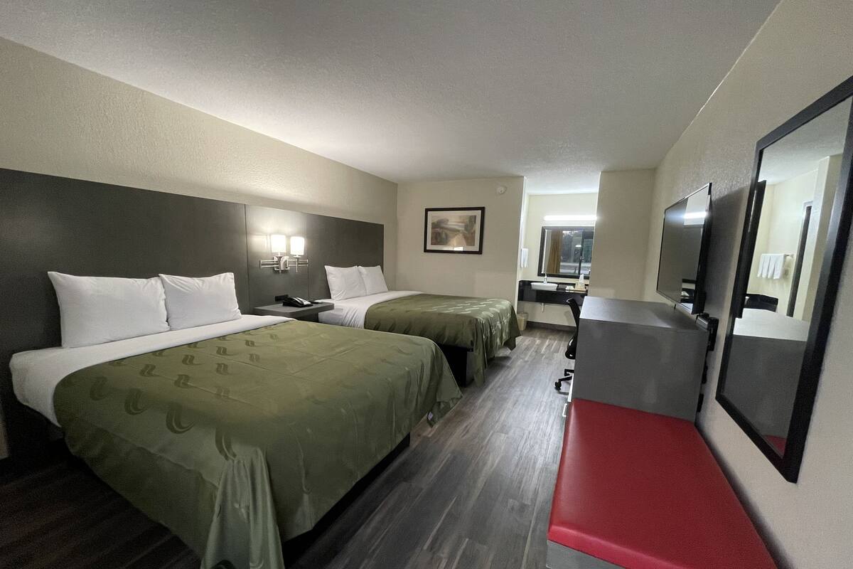 A hotel room with two beds, a desk, a chair, a TV, and a mirror.