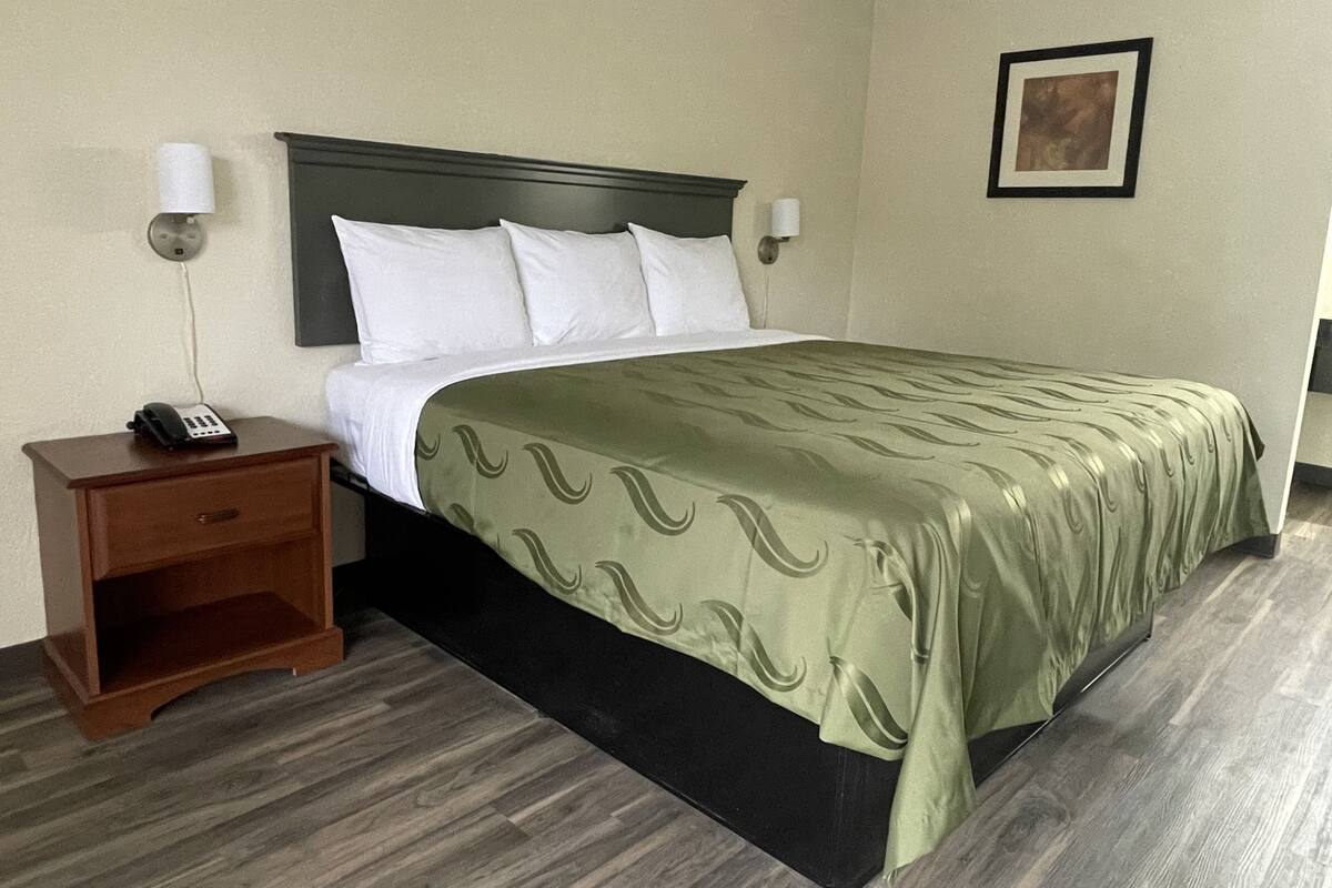 A hotel room with a bed, a nightstand, a telephone, and a framed picture on the wall.