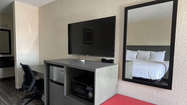 Habitación de hotel con cama, escritorio, computadora, silla, televisor y espejo.