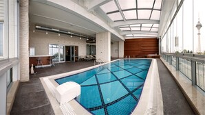Una piscina interior con suelo de baldosas, pared de madera y techo de cristal.