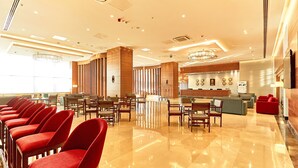 Un vestíbulo de hotel con una hilera larga de sillas rojas, un mostrador de recepción y una lámpara de araña moderna.