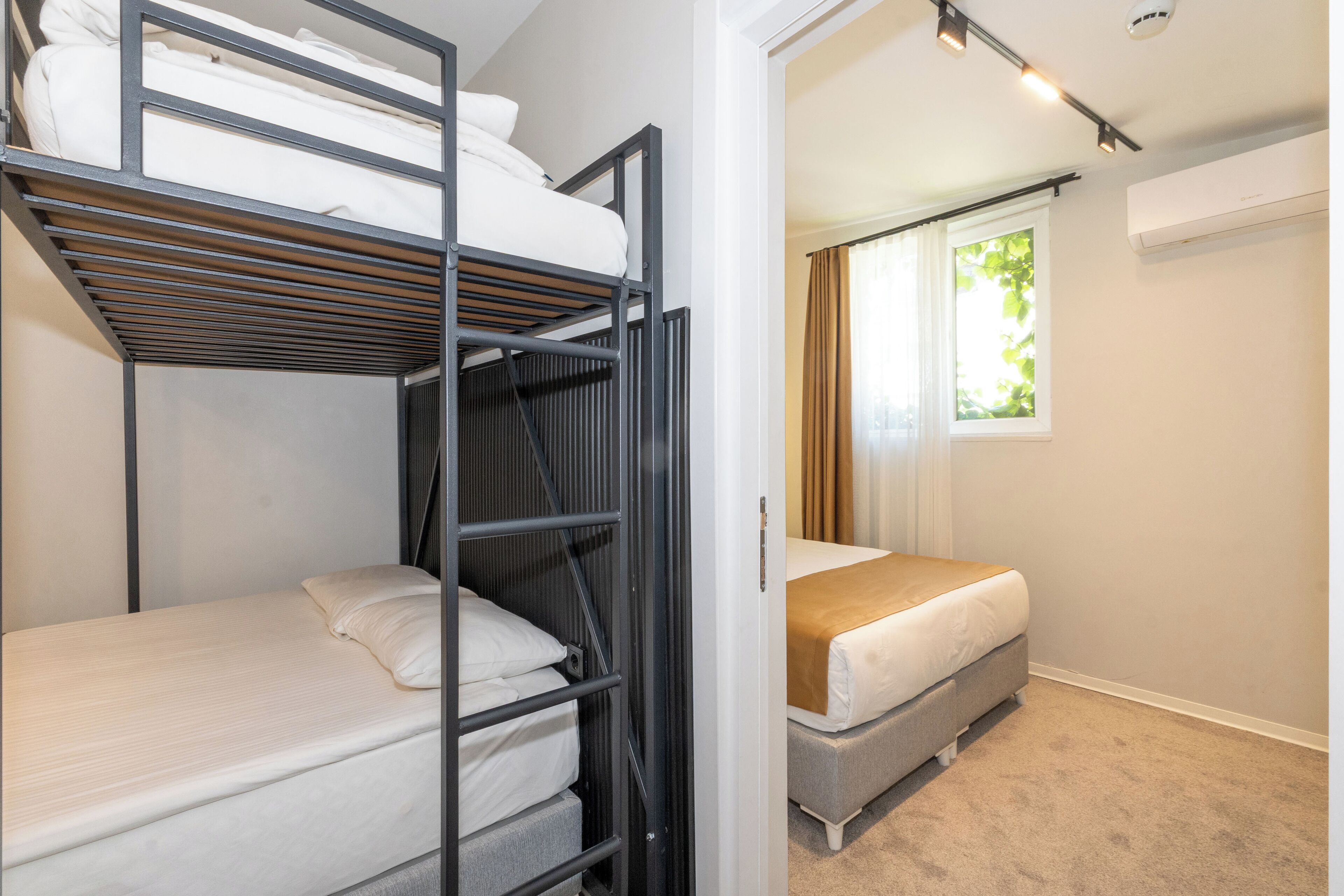 A room with a bunk bed, a single bed, and a window with curtains.