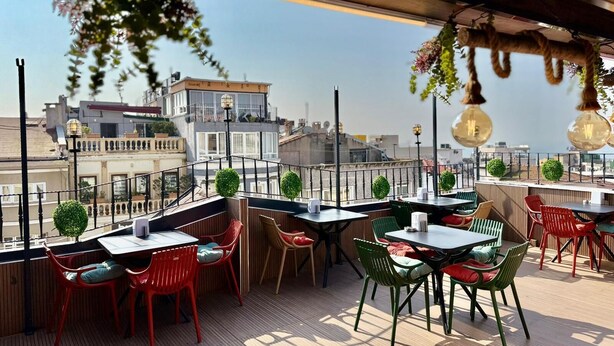 A rooftop terrace with tables and chairs, a view of the city, and hanging plants. - Istanbul Holiday Hotel (Istanbul)