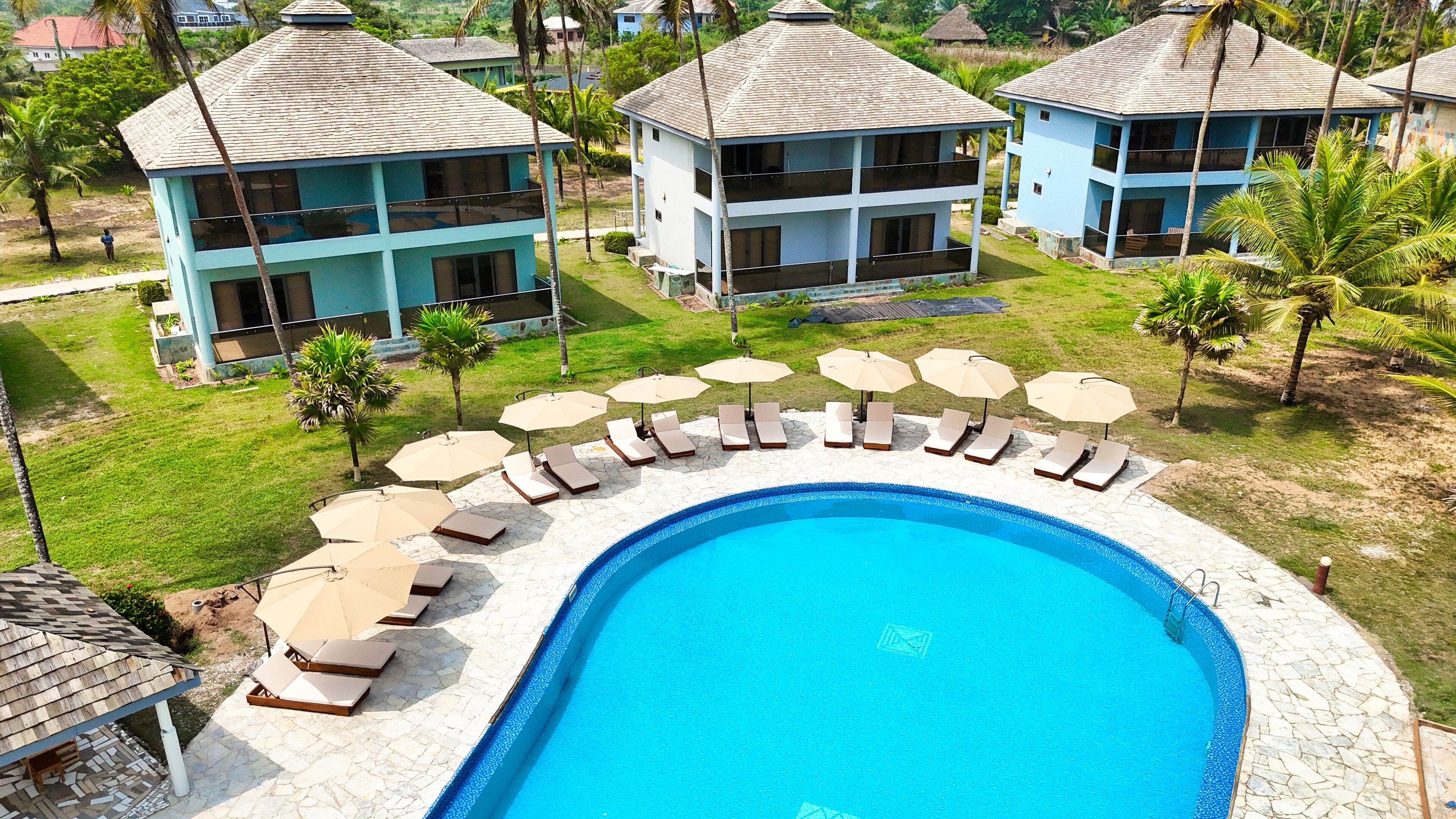 Zona de piscina con sillas de descanso y sombrillas, rodeada de edificios con balcones.