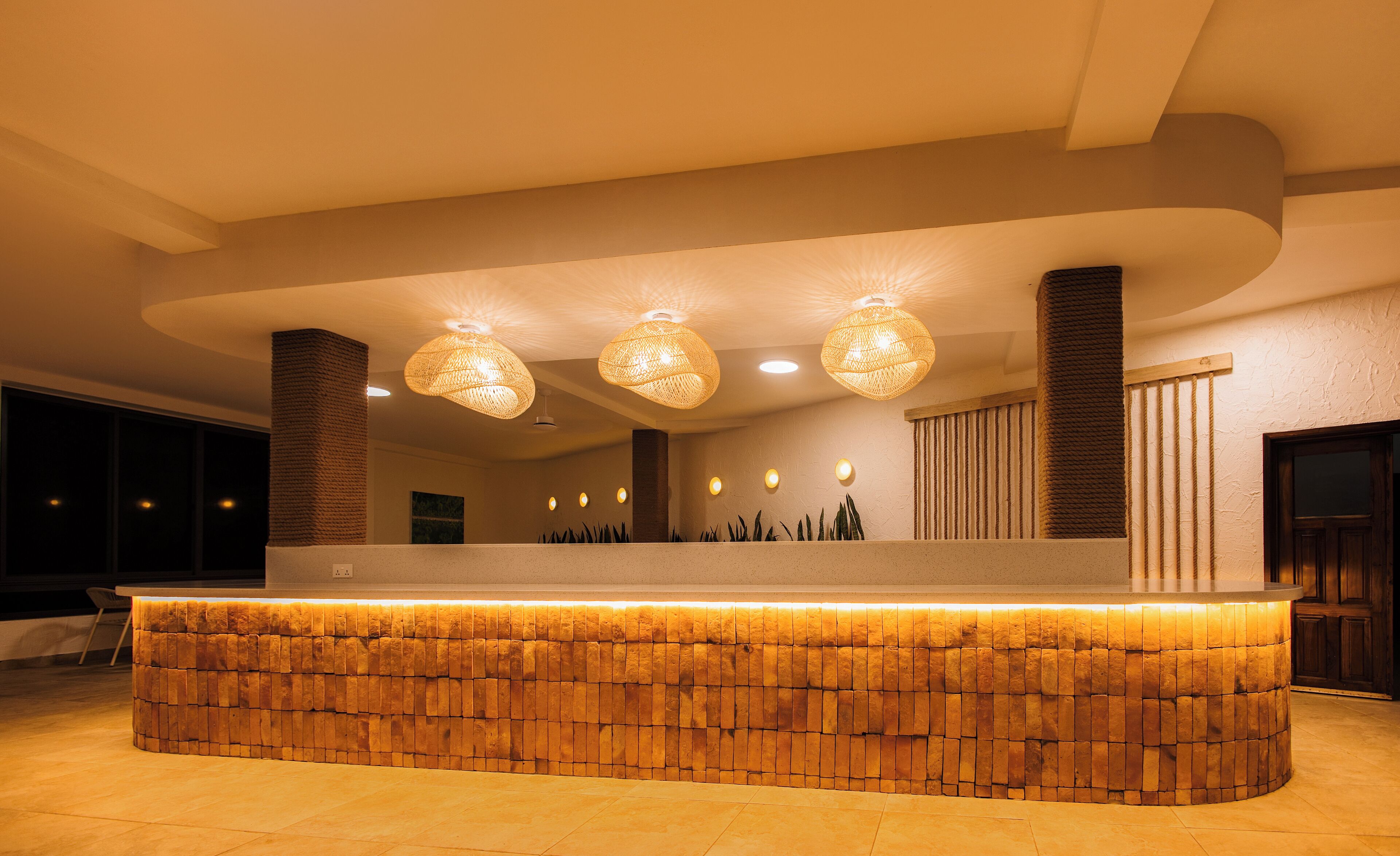 A reception area with a stone-textured counter, three woven pendant lights, and a wooden column.