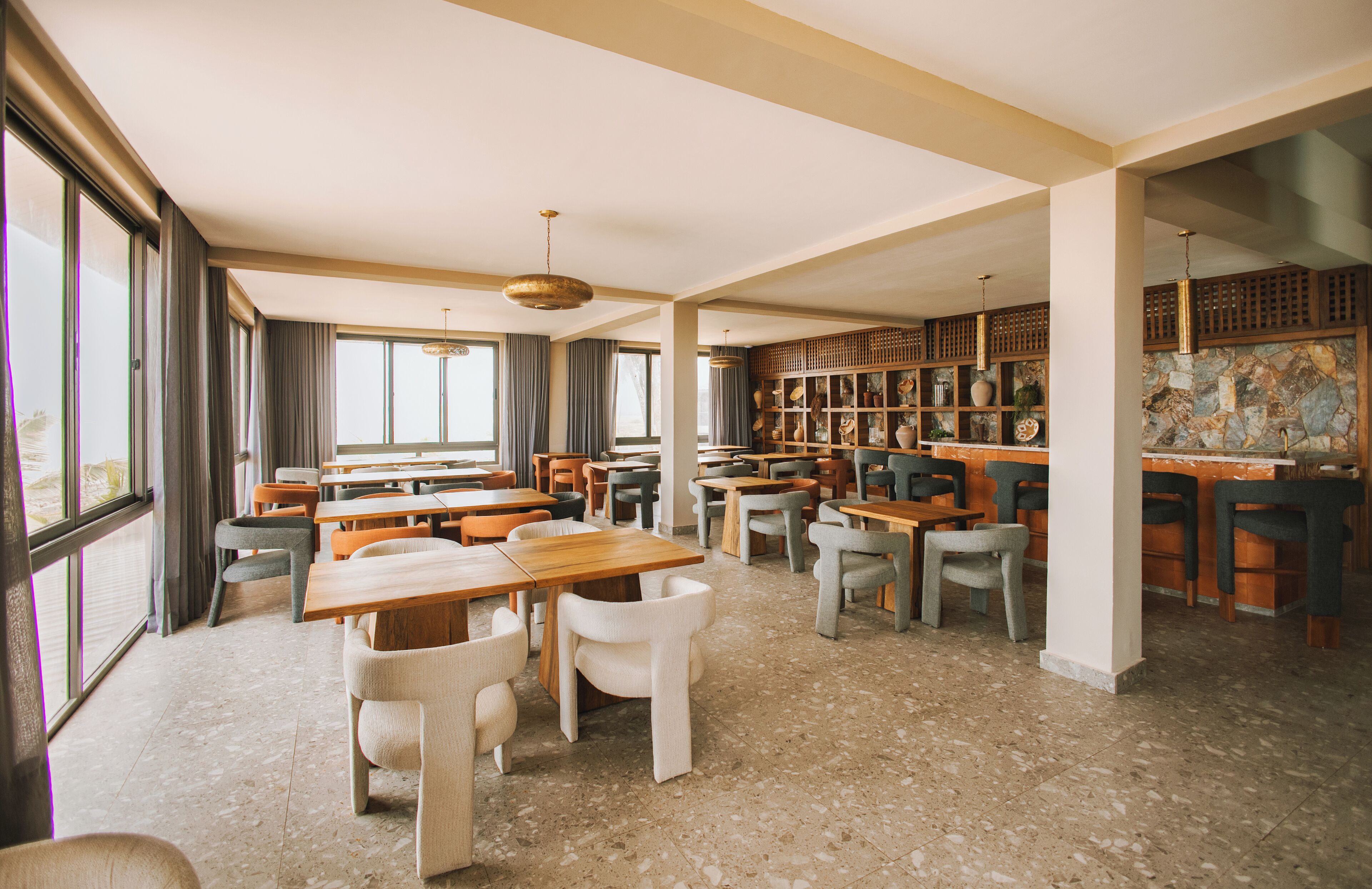 A spacious dining area with multiple tables and chairs, large windows, and a decorative wall with shelves.