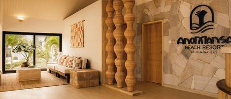 A modern lobby with a stone wall, a wooden reception desk, and a sofa with cushions.