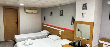 A hotel room with two single beds, a small desk with a kettle, and a mirror.