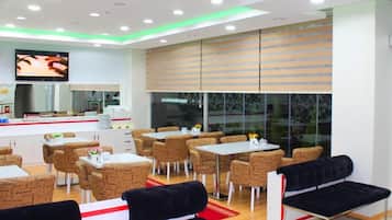 A modern dining area with tables and chairs, a counter with a display, and a television mounted on the wall.