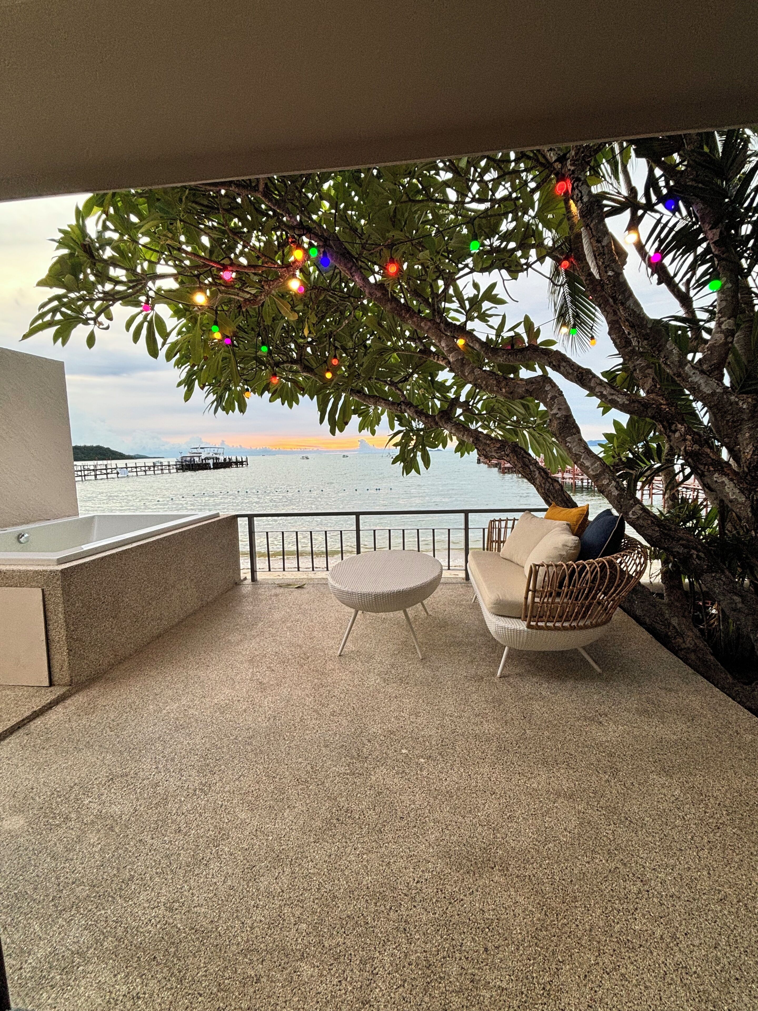 A balcony with a view of the sea, a wicker chair, a small round table, and string lights.