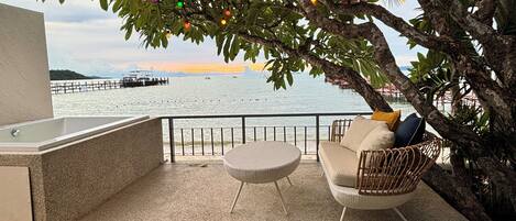 A balcony with a view of the sea, a wicker chair, a small round table, and string lights.