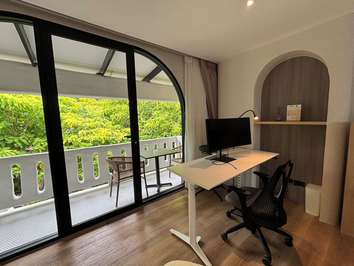 Un espacio de oficina moderno con escritorio, silla y computadora. Cuenta con ventanas amplias que dan a zonas verdes.