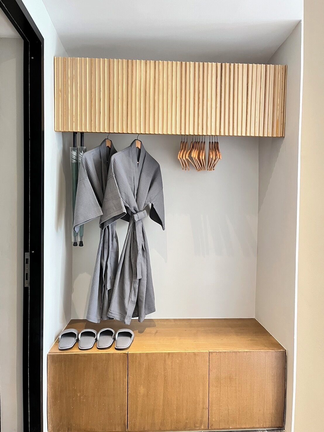 Un baño moderno con tocador de madera, dos toallas y un par de zapatillas.