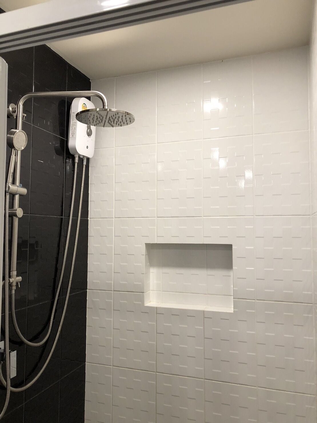 Un espace douche équipé d’un pommeau de douche à main, d’un panneau de commande fixé au mur et d’une petite étagère.