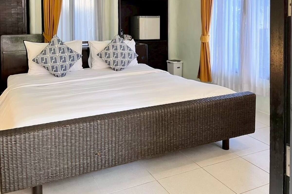 A hotel room with a large bed, a wardrobe, a flat-screen TV, and a ceiling-mounted air conditioner.