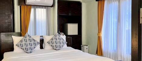 A hotel room with a large bed, a wardrobe, a flat-screen TV, and a ceiling-mounted air conditioner.