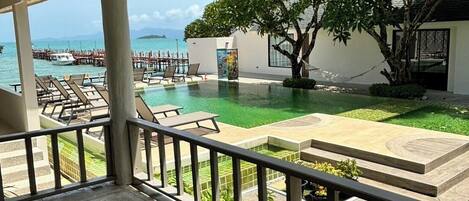 A covered outdoor area with a pool, lounge chairs, and a view of the sea and dock.