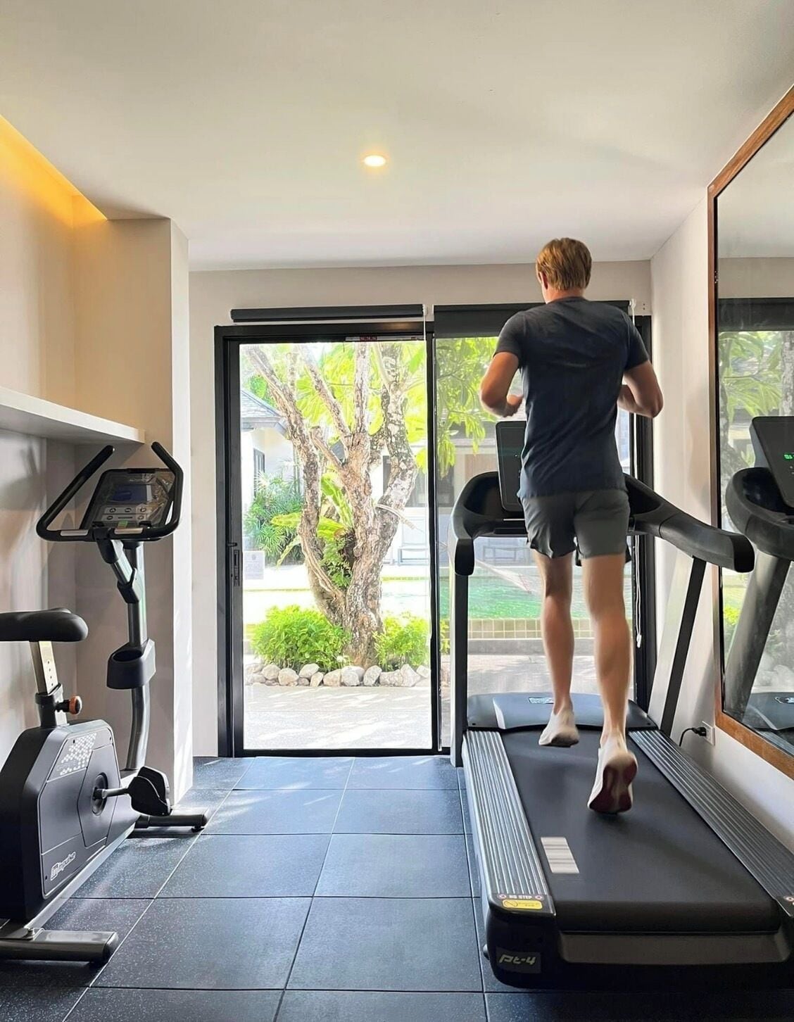 Un gimnasio moderno con cinta de correr, bicicleta estática y un espejo grande.