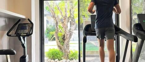 Un gimnasio moderno con cinta de correr, bicicleta estática y un espejo grande.