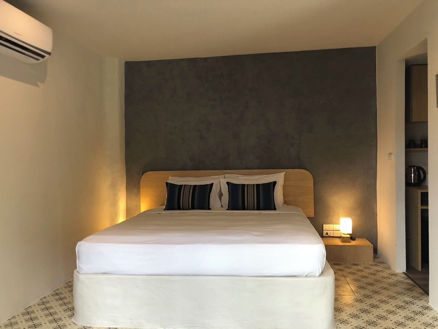 Een hotelkamer met een bed, een nachtkastje met een lamp en een wandairconditioner.