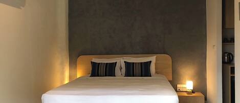 Een hotelkamer met een bed, een nachtkastje met een lamp en een wandairconditioner.