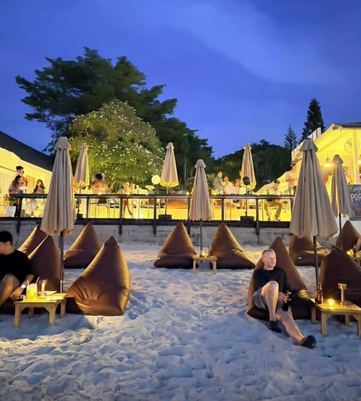 An outdoor seating area with bean bags and umbrellas, a bar area with people, and a view of the sky.