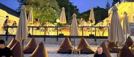 An outdoor seating area with bean bags and umbrellas, a bar area with people, and a view of the sky.
