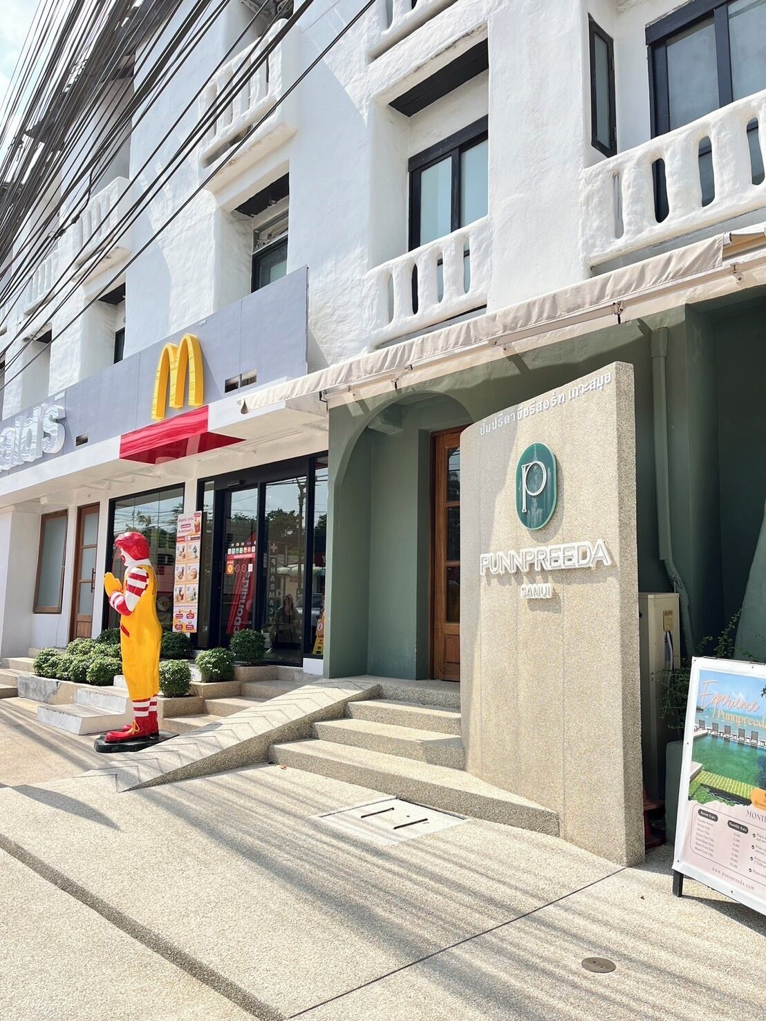 A hotel entrance with a McDonald's sign, a statue of Ronald McDonald, and a sign for PUNPREEDA.