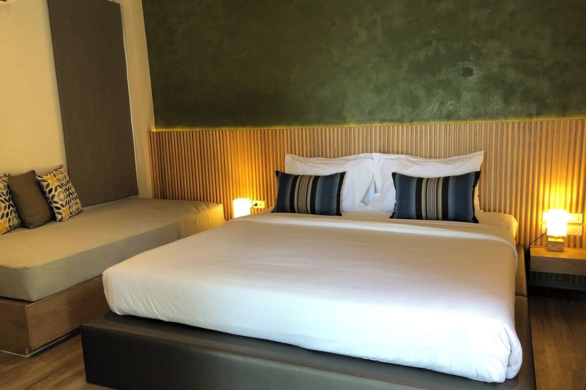 A modern hotel room with a large bed, a sofa, and a small table with a lamp.