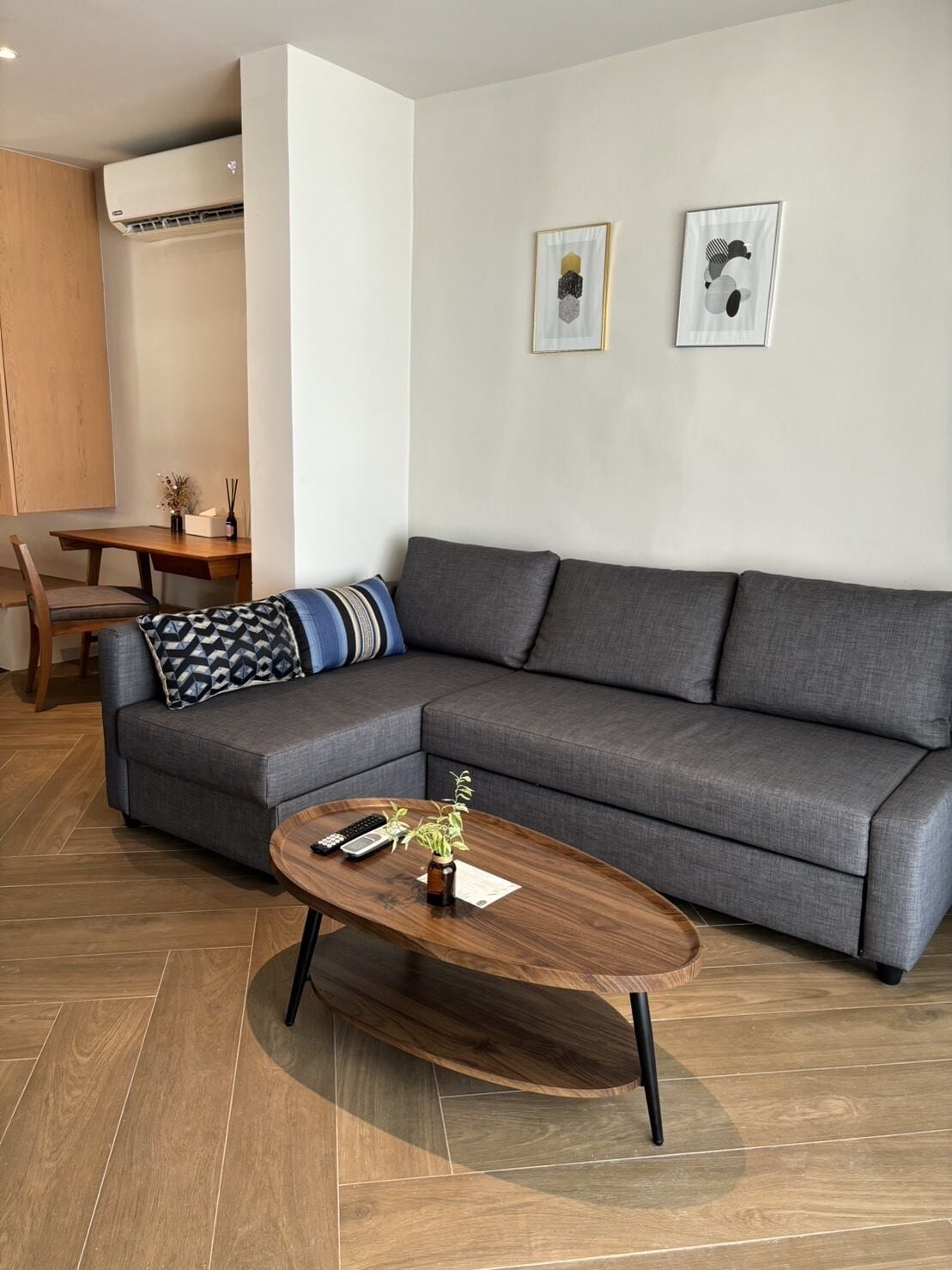 Un salon moderne avec un canapé d’angle gris, une table basse en bois et un coin repas comprenant une table et des chaises en bois.