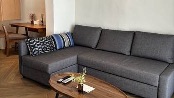 Un salon moderne avec un canapé d’angle gris, une table basse en bois et un coin repas comprenant une table et des chaises en bois.