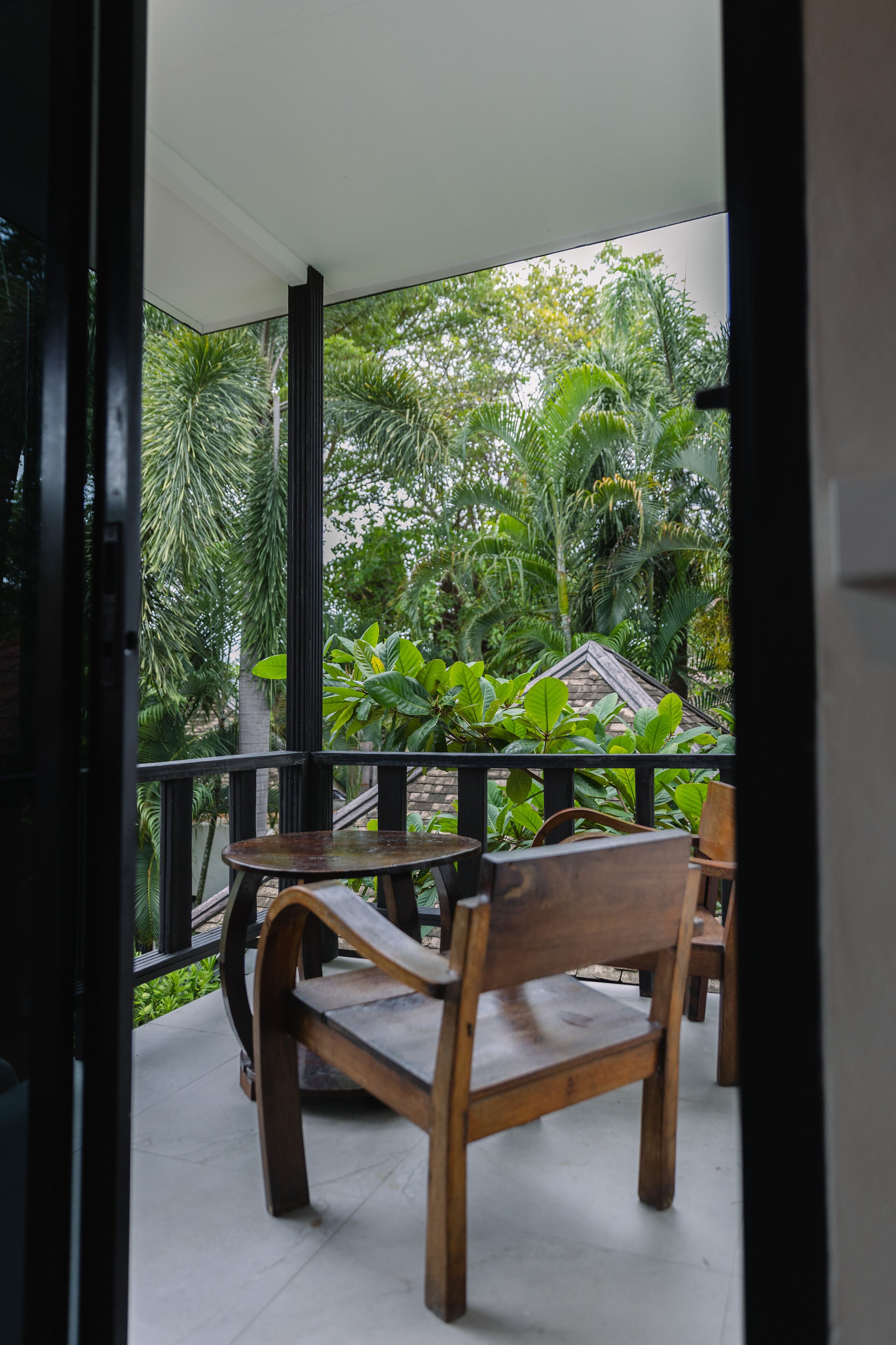 A balcony with wooden furniture, surrounded by lush greenery and a view of a house.