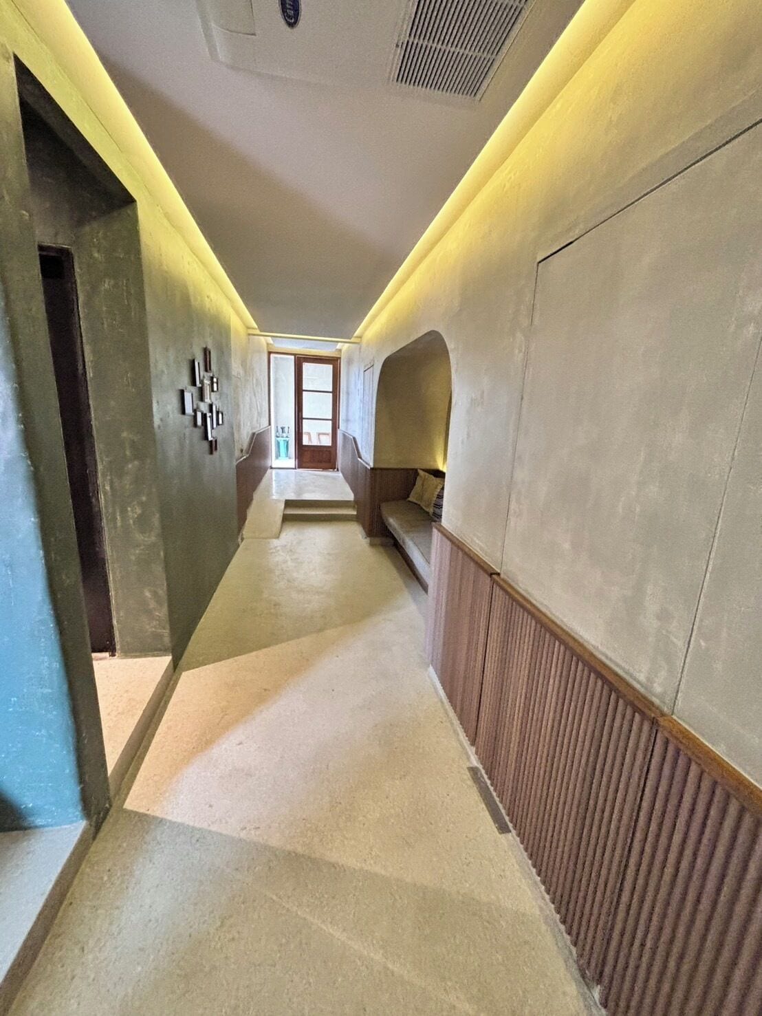 A hallway with a wooden bench, a door at the end, and a wall-mounted light fixture.