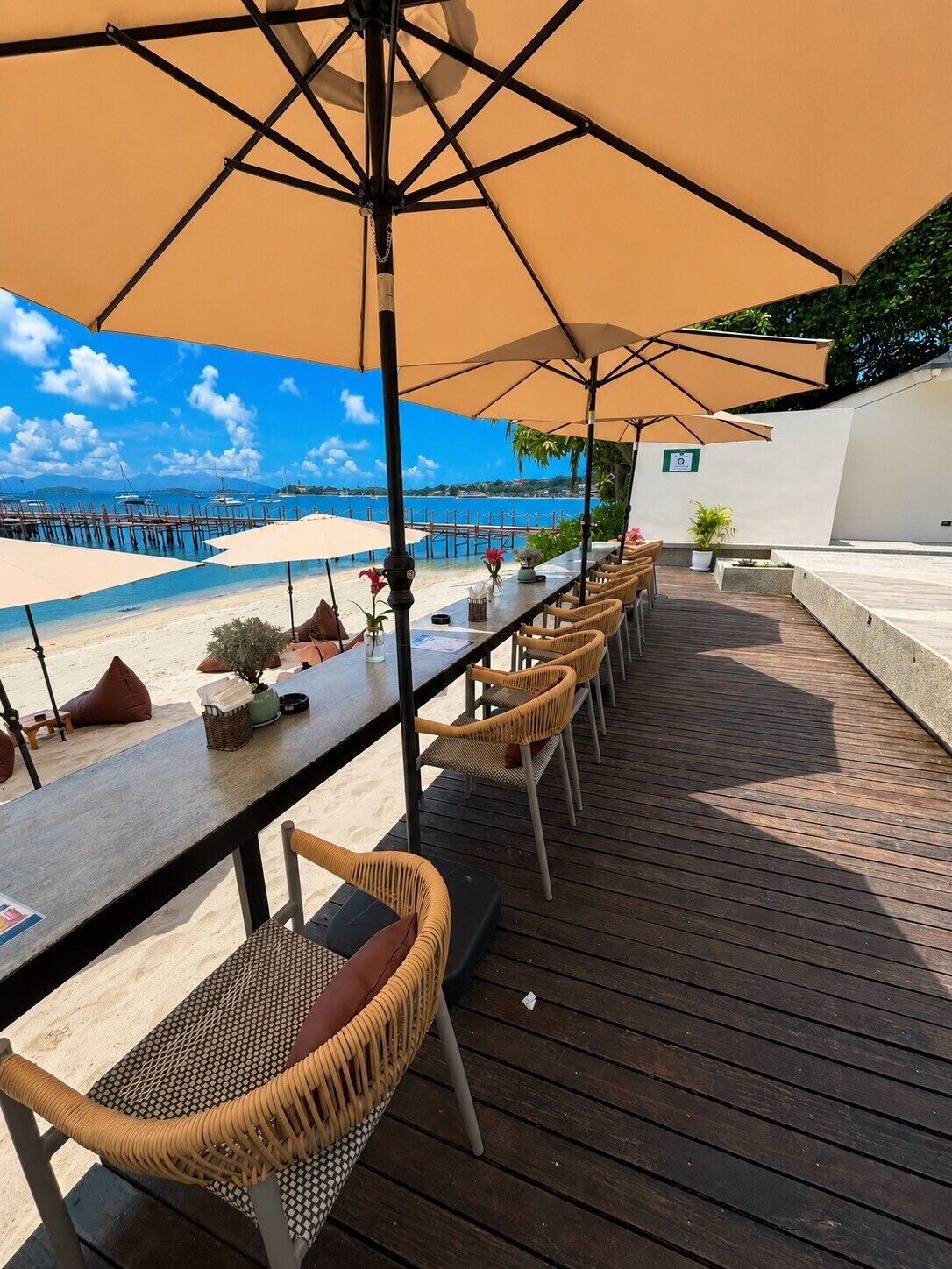 A wooden deck with outdoor seating and umbrellas overlooking a beach and pier.