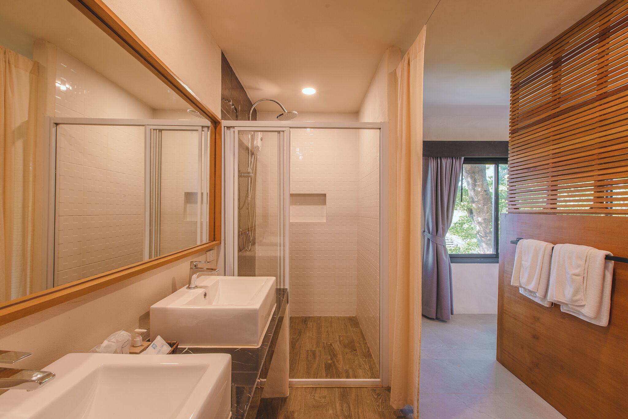 A modern bathroom with two sinks, a shower, and a wooden vanity.
