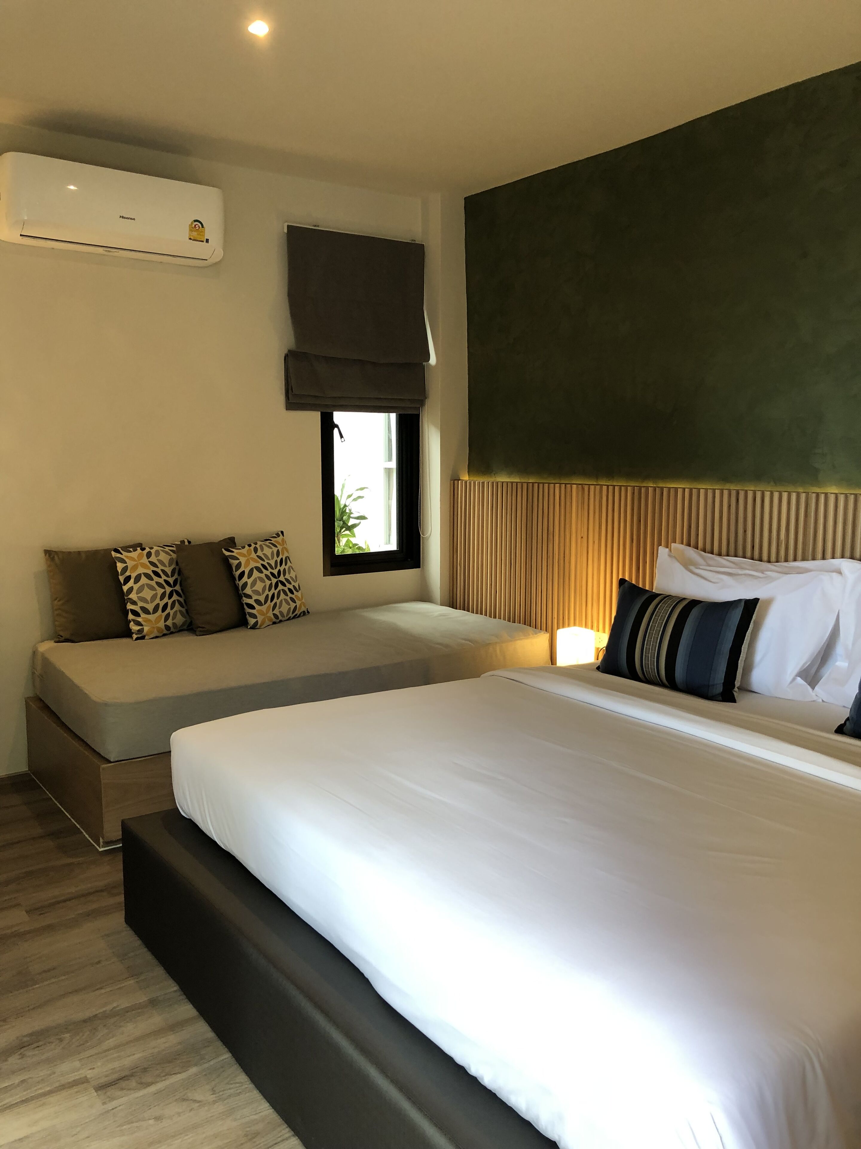 Una habitación de hotel moderna con una cama grande, un sofá cama, un ventanal con vistas y un equipo de aire acondicionado.