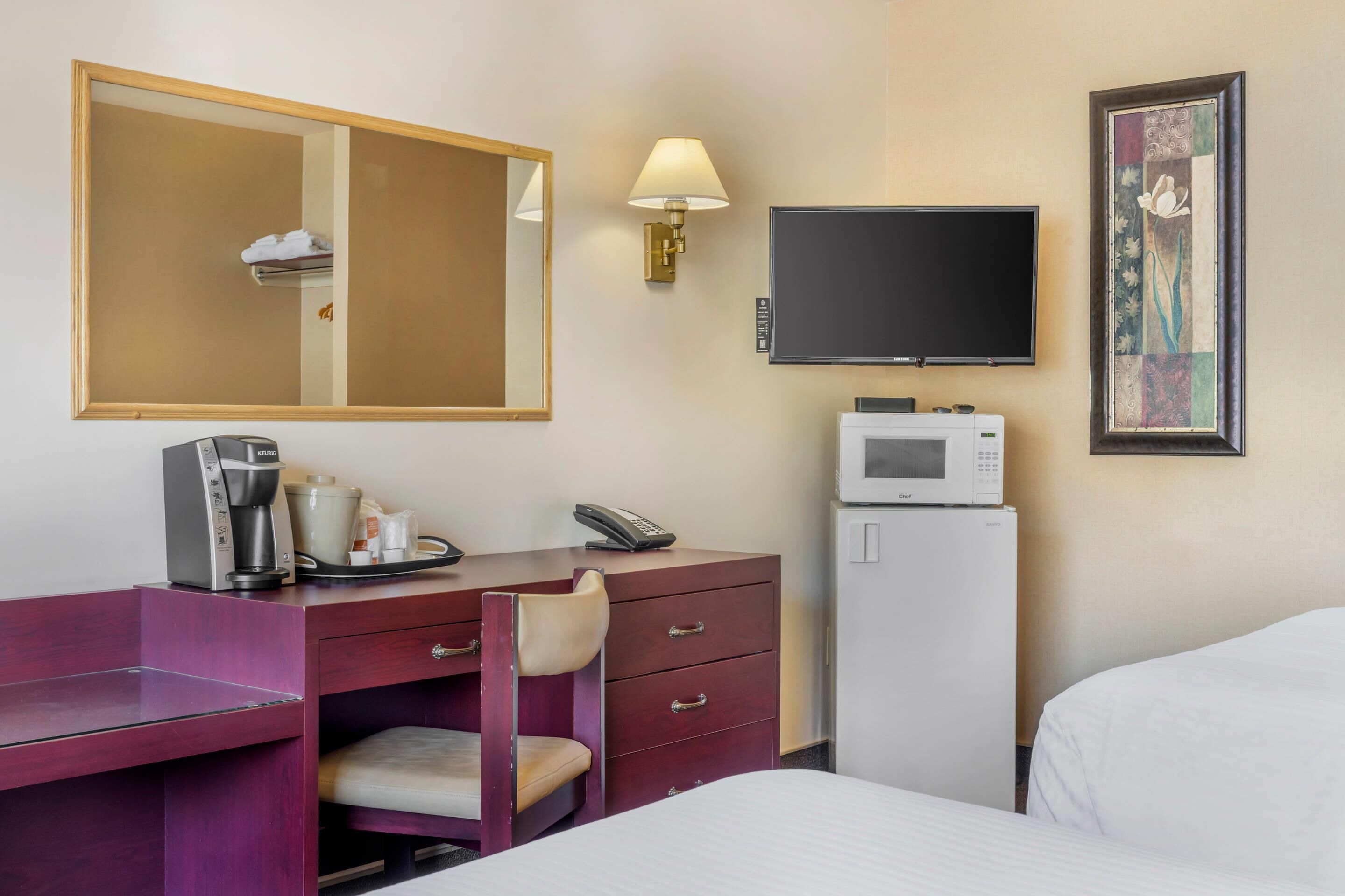 A hotel room with a desk, a chair, a bed, a television, a microwave, and a refrigerator.