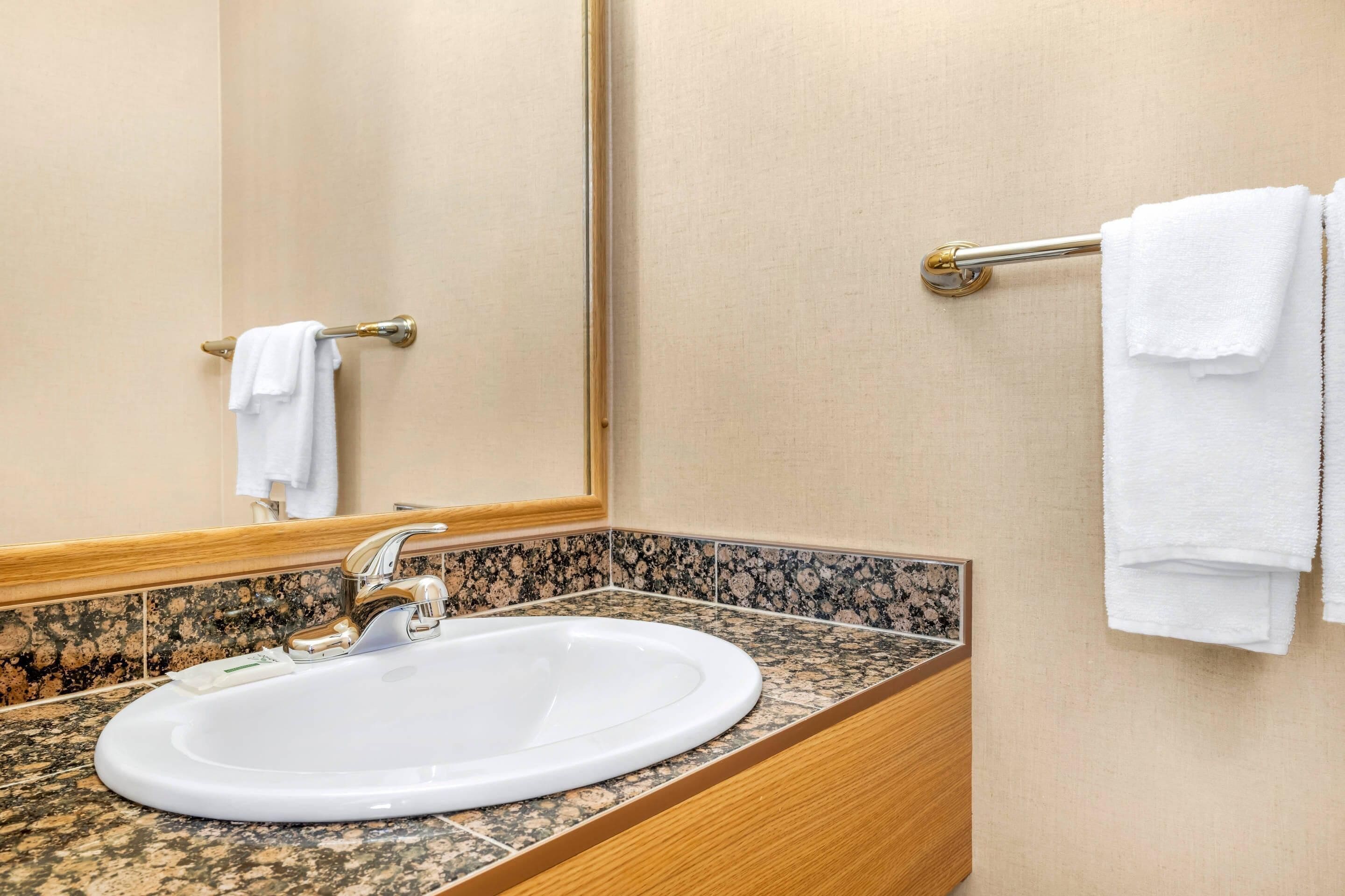 Un bagno con un lavandino bianco, uno specchio e un portascopevoli con asciugamani bianchi.