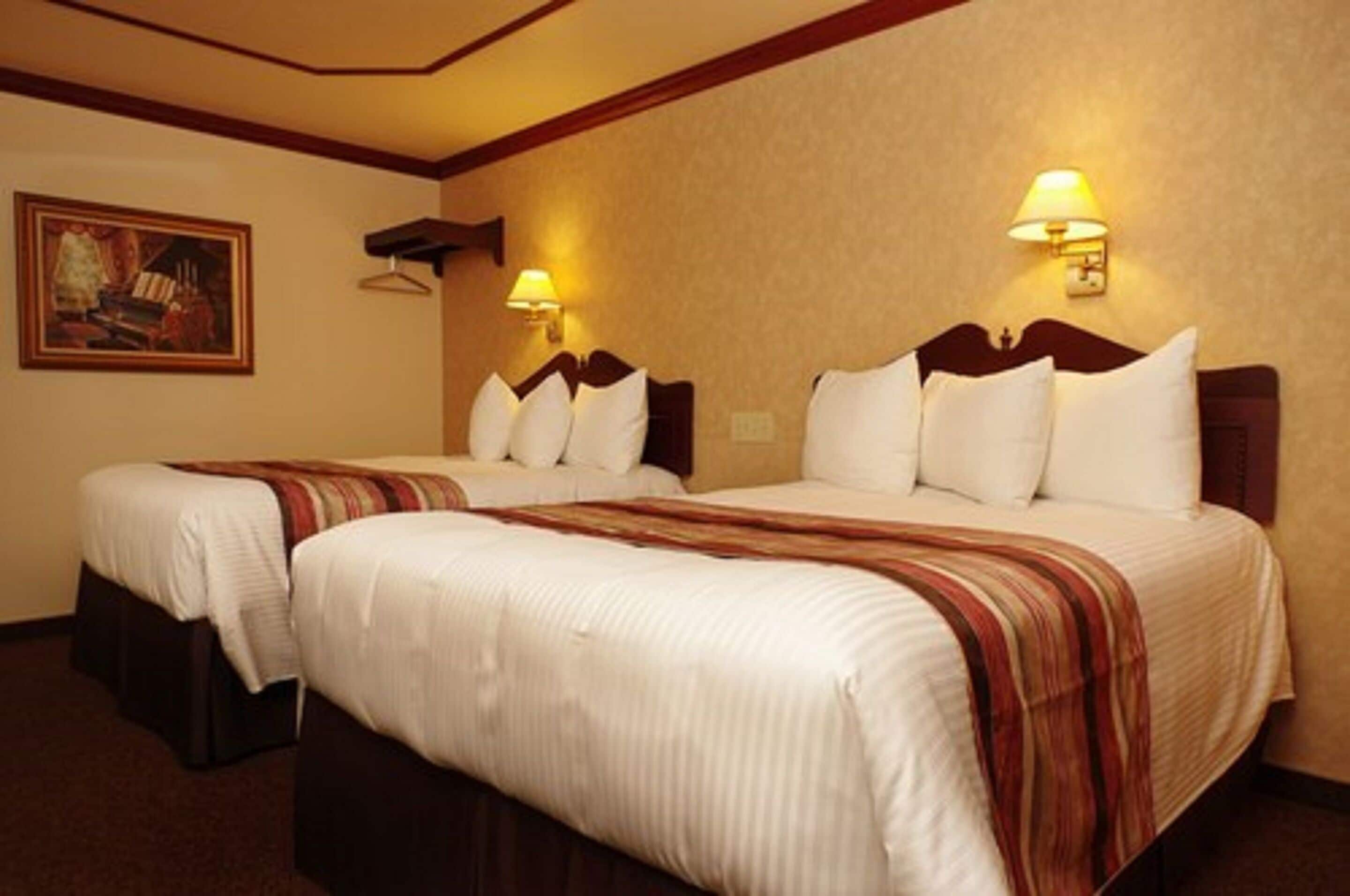 Una habitación de hotel con dos camas, cada una con ropa blanca y mantas a rayas. Hay lámparas de pared y un cuadro en la pared.