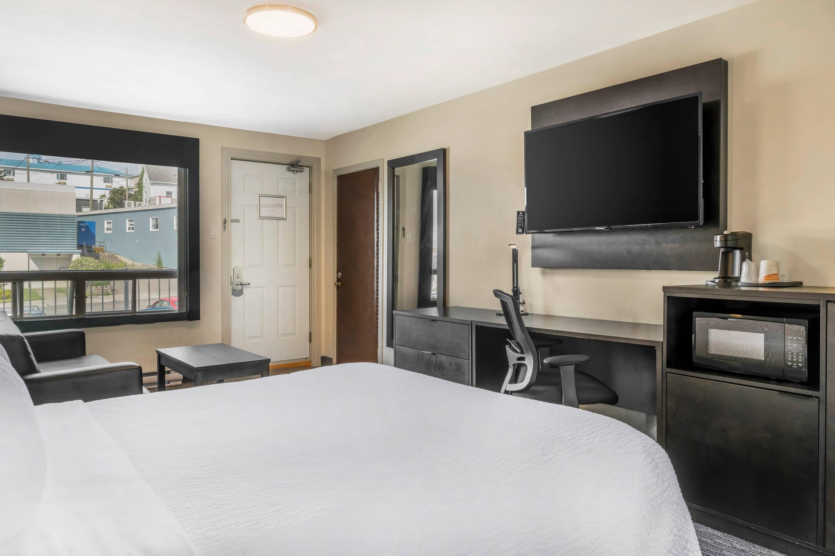 Una habitación de hotel con cama, escritorio, silla, televisor y cafetera.
