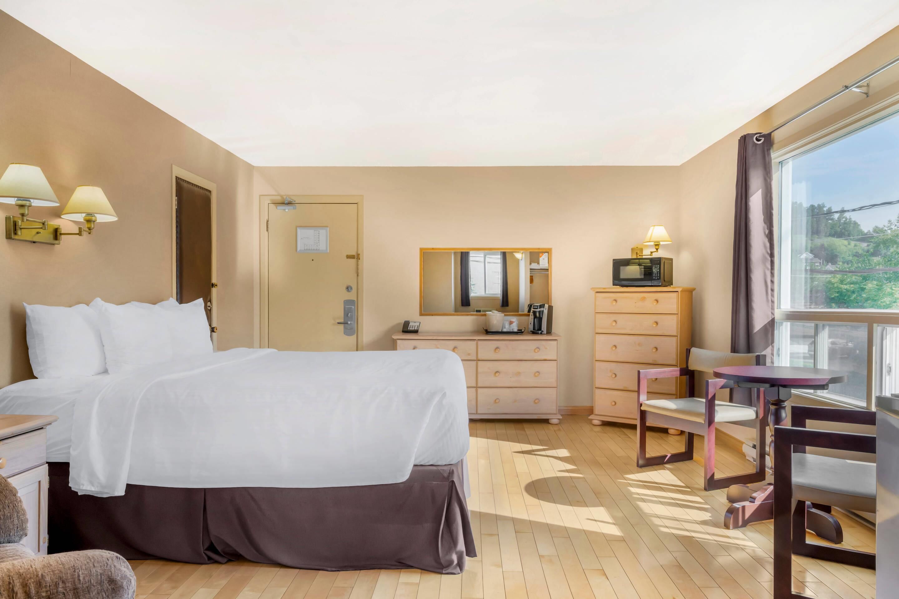 A hotel room with a bed, dresser, mirror, and a table with chairs.