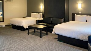 A hotel room with two beds, a sofa, a small table, and two wall-mounted lights. - Rodeway Inn (Gaspé)