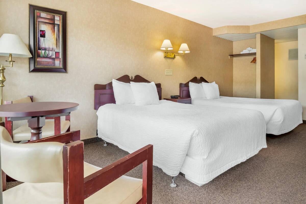 A hotel room with two beds, a desk, a chair, and a lamp.