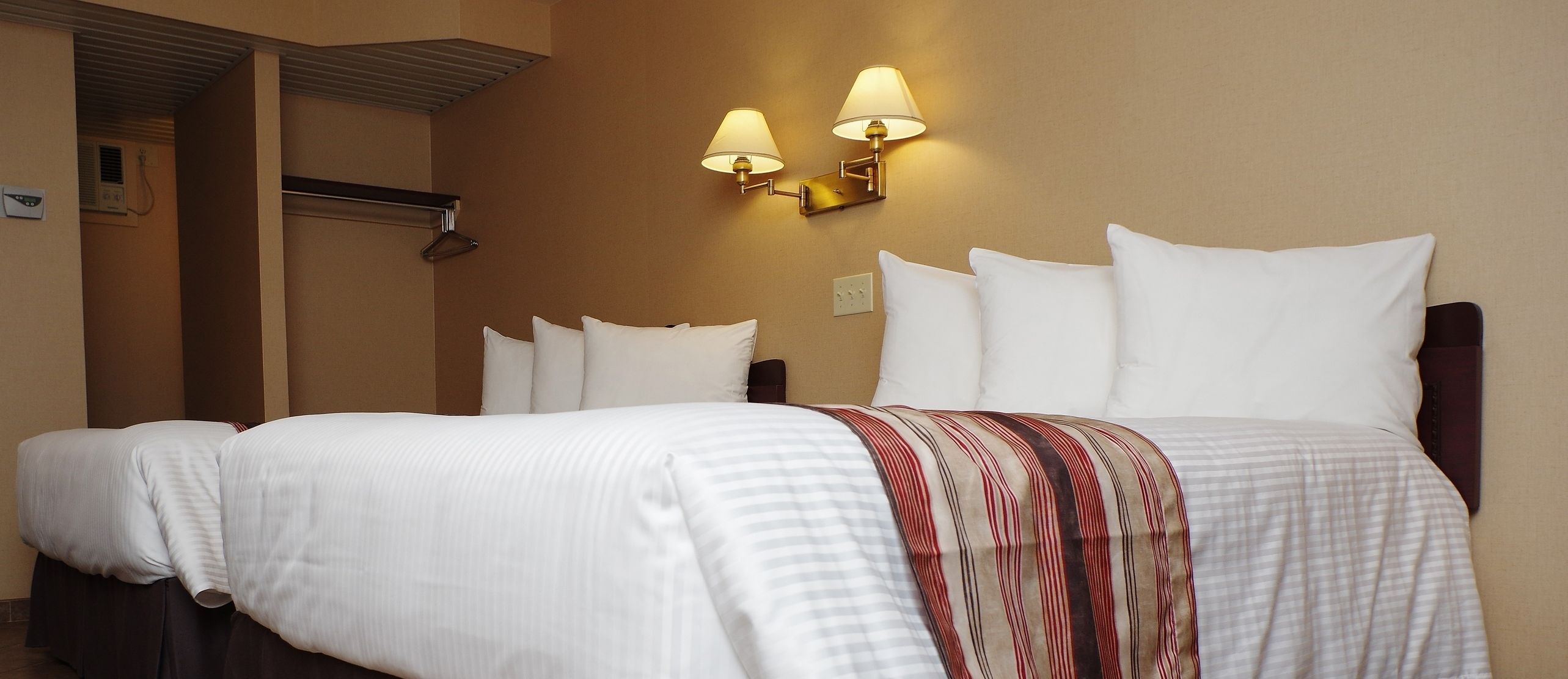 A hotel room with a double bed, two wall-mounted lamps, a headboard, and a bedside table.