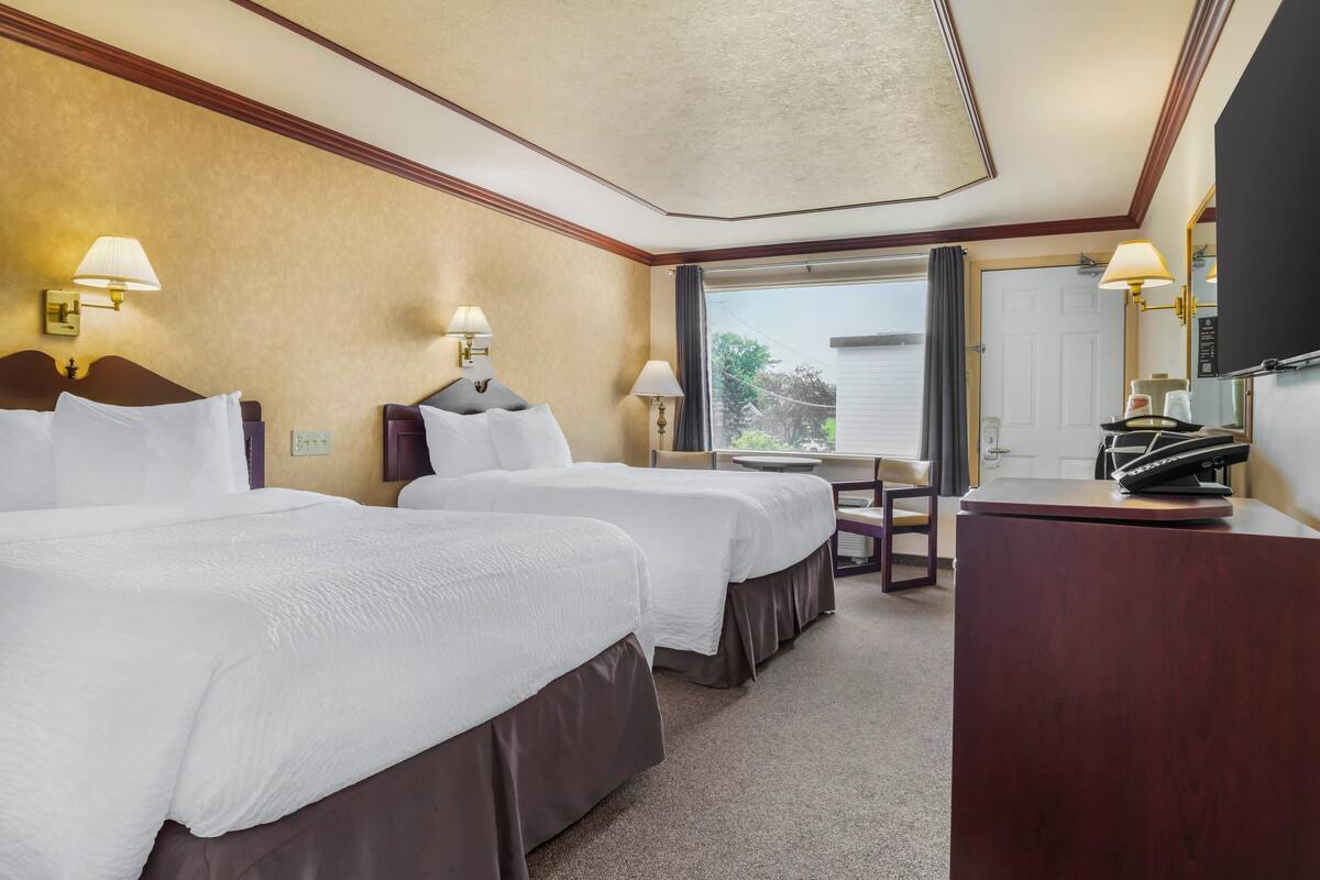 A hotel room with two beds, a desk, a chair, a TV, and a window with a view.
