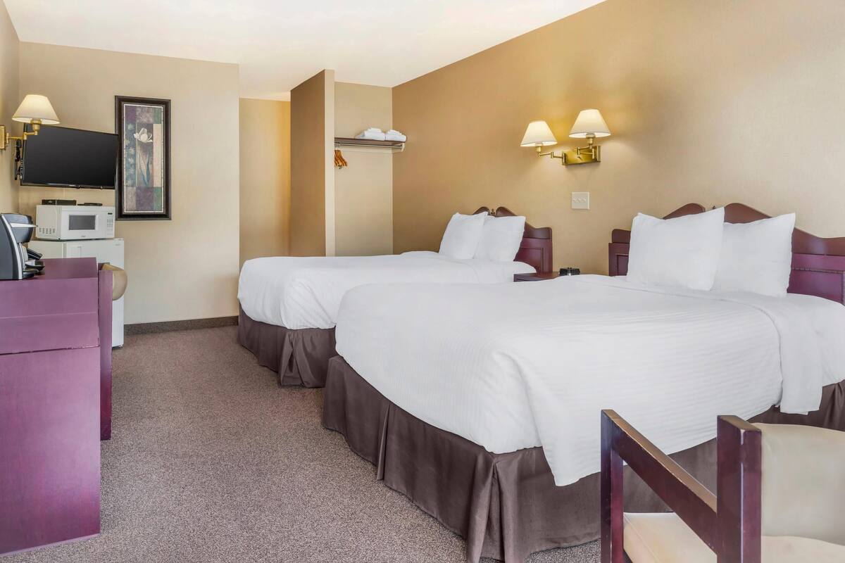 A hotel room with two beds, a desk with a computer, a TV, and a microwave.